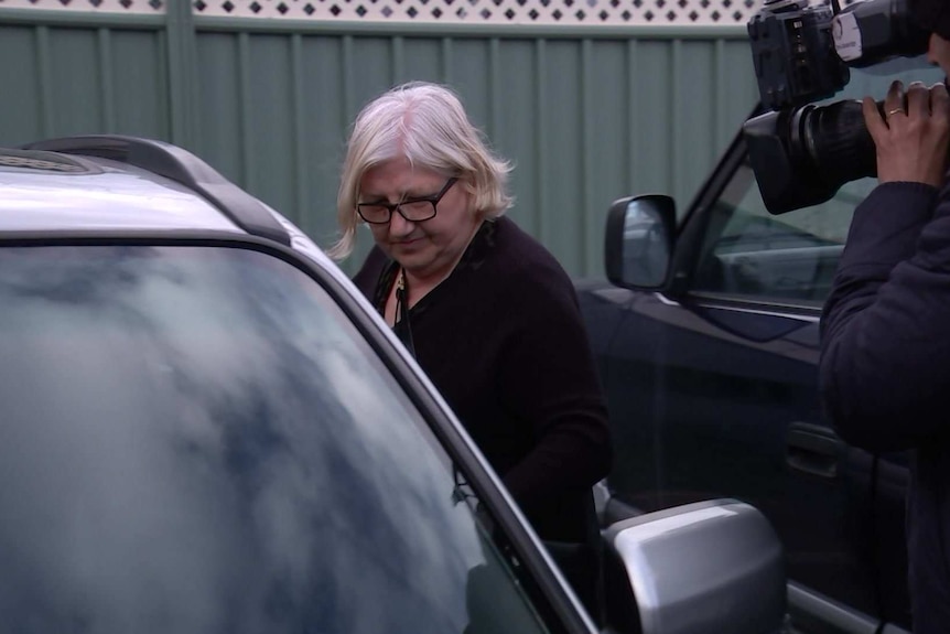 A woman gets into a car as a television camera records her.