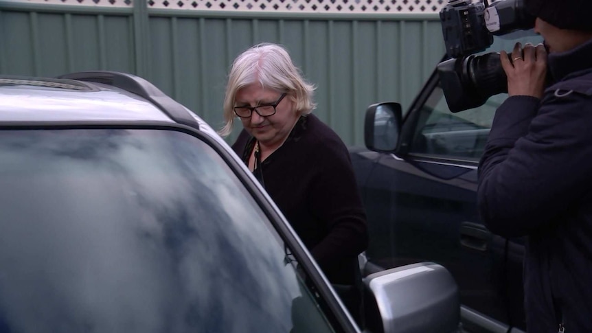 A woman gets into a car as a television camera records her.