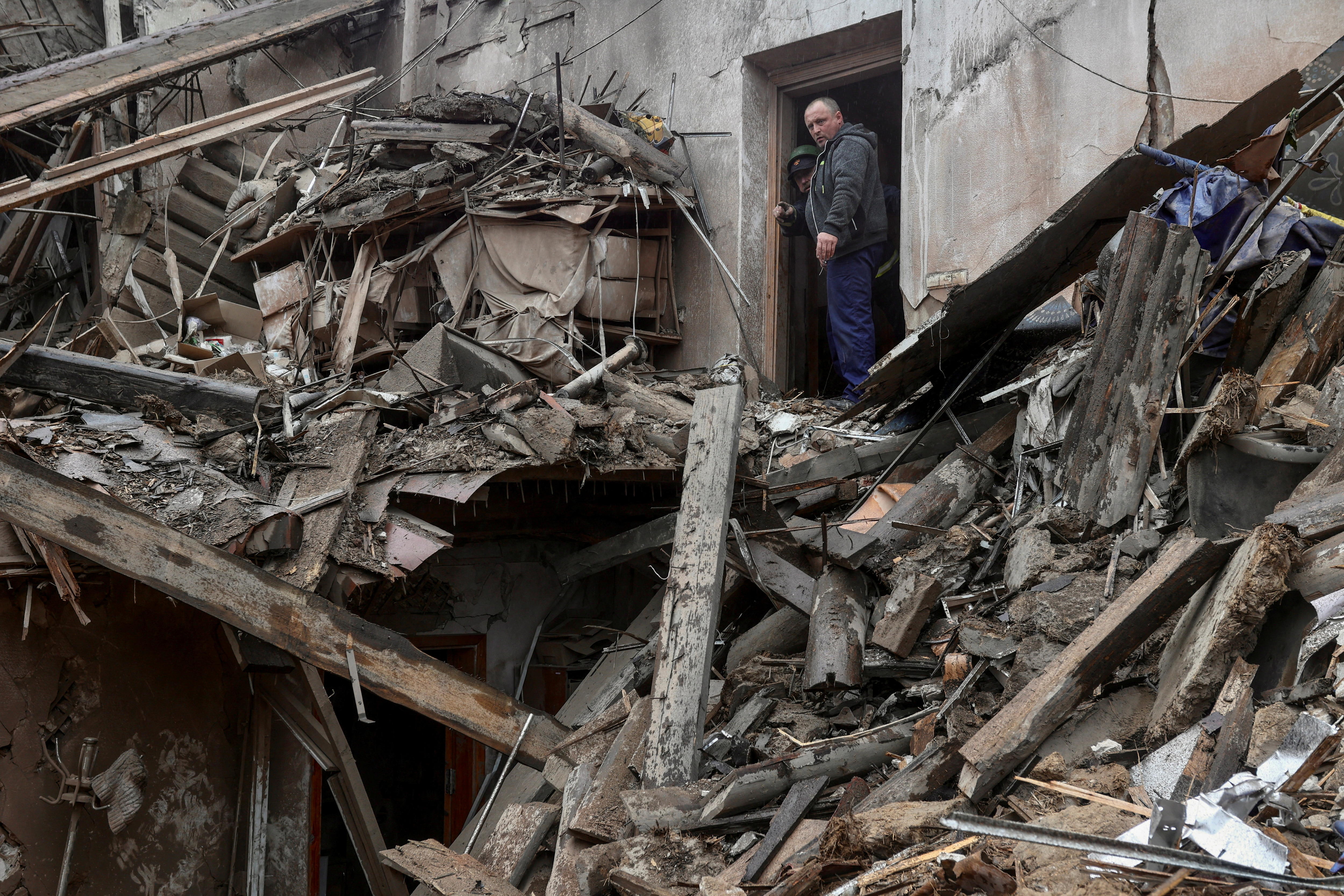 Two man stand in a destroyed doorway overlooking a pile of rubble that was once a museum.