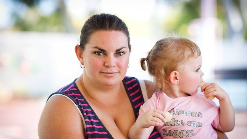 A mother holding her daughter, who is eating potato chips.