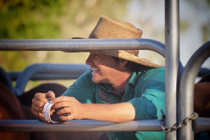 A close up of a grazier leaning against fencing smiling