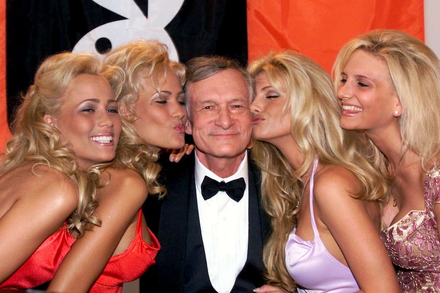 Hugh Hefner smiles in the middle of four blond Playboy playmates.