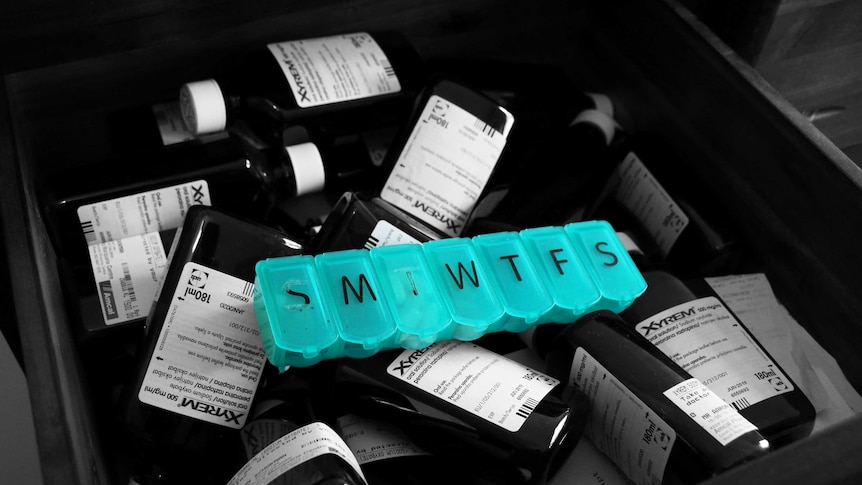 A black and white photo of a drawer full of empty Xyrem medication bottles, a pill box sits in the middle in full colour