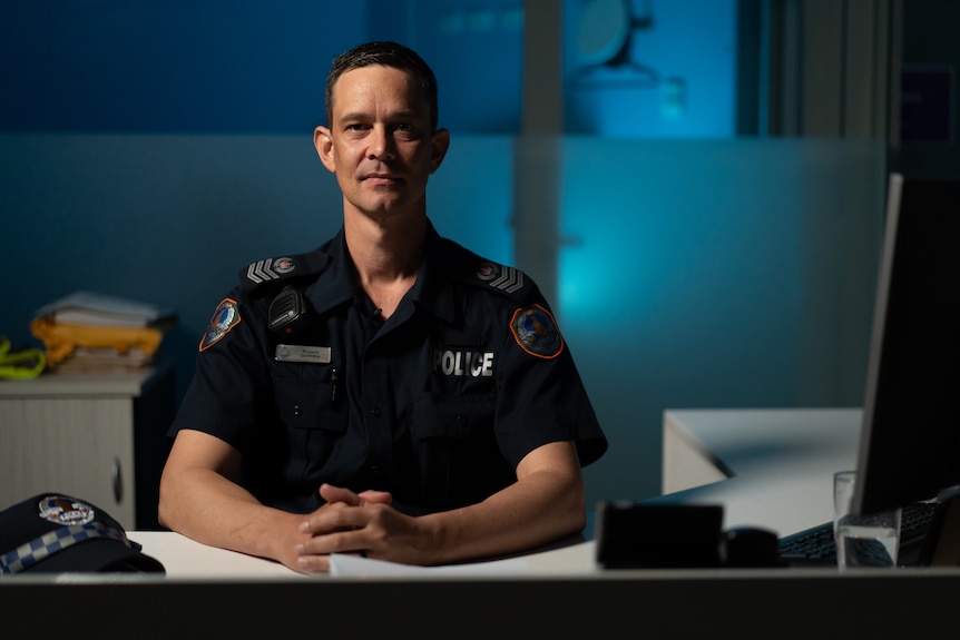 A man wearing a police uniform sitting at a desk.