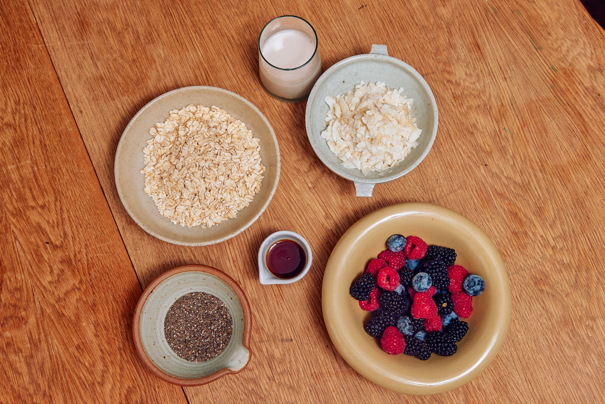 Oats, chia seeds, almond milk, maple syrup, coconut flakes and berries, ingredients for overnight oats.