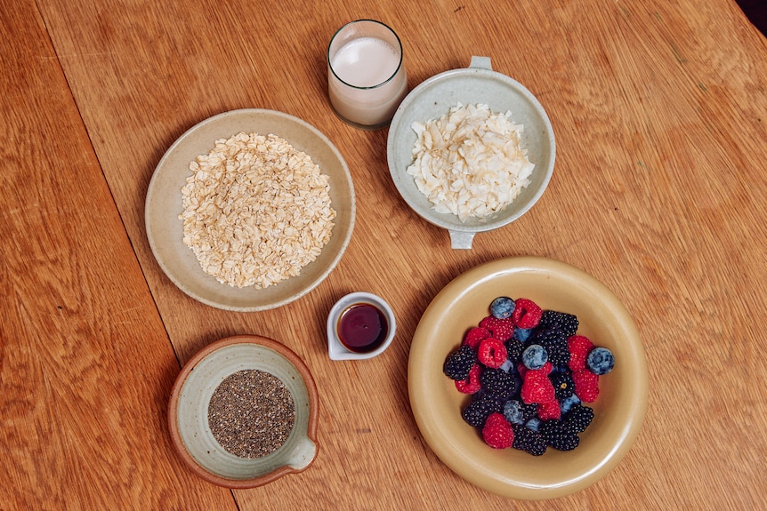 Oats, chia seeds, almond milk, maple syrup, coconut flakes and berries, ingredients for overnight oats.