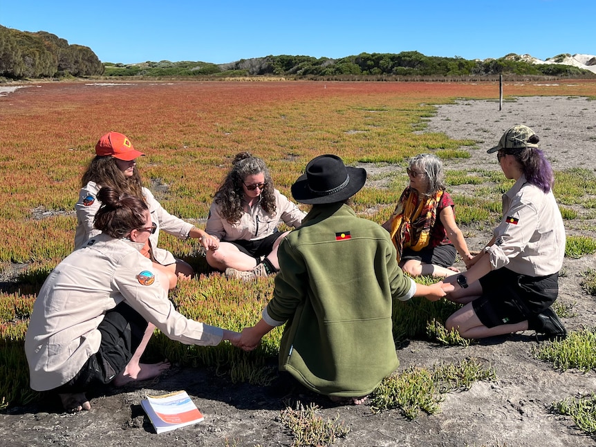 A group of women sit on open grassland with blue sky,