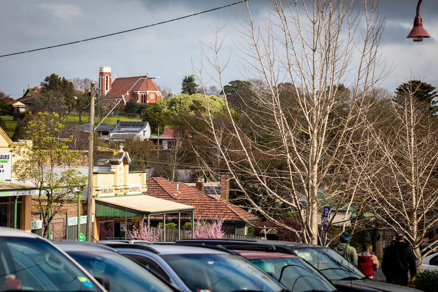 Small town shops, parked cars, Anglican church in background