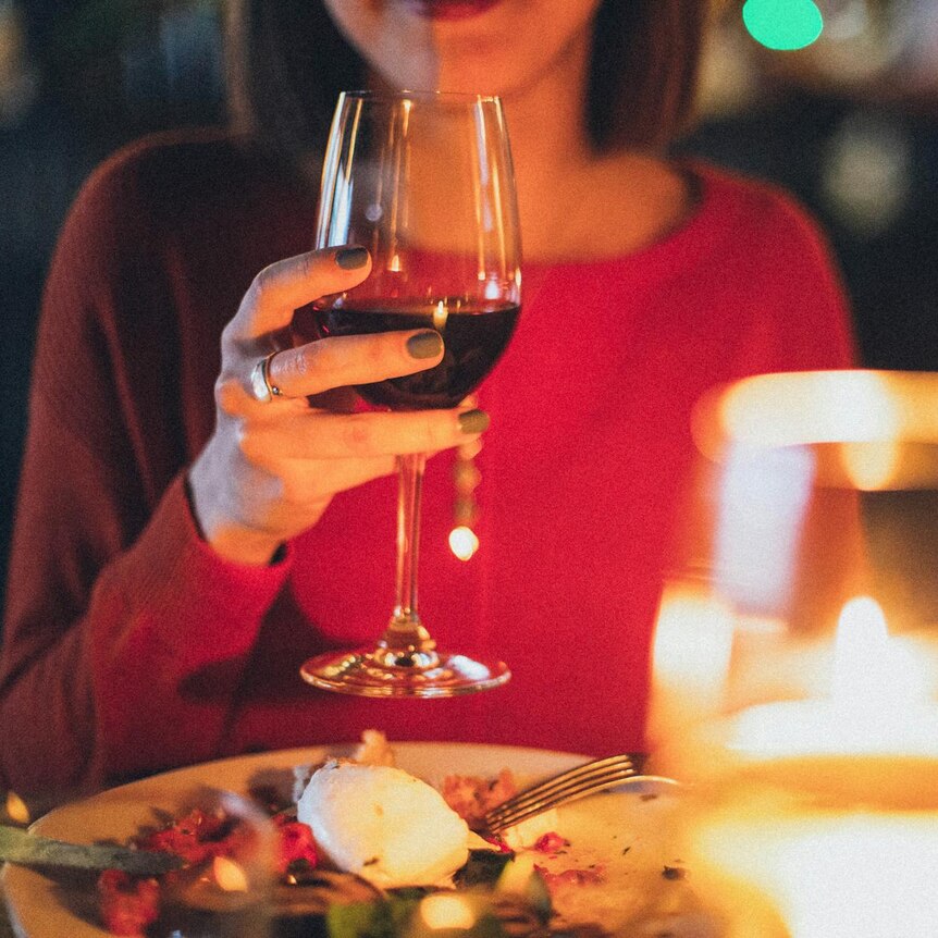 Photo of a woman raising a glass of red wine to her lips at a restaurant table