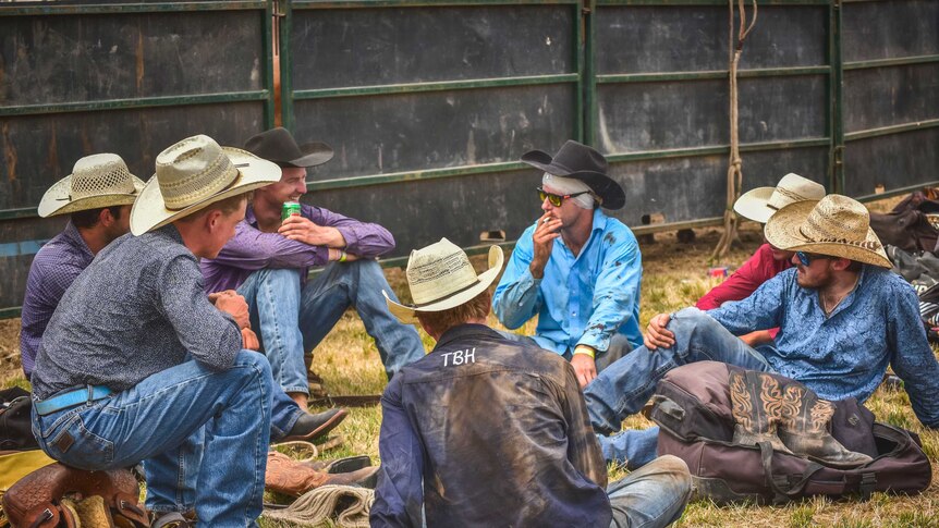 A group of cowboys sit in a circle chatting after a rodeo event.