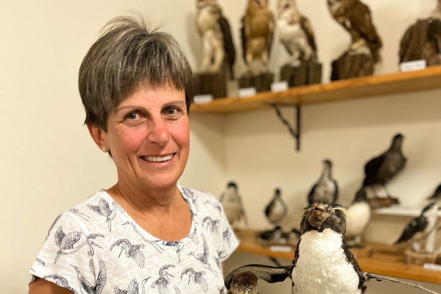 A lady in a bird motif shirt holds a taxidermied penguin and chick