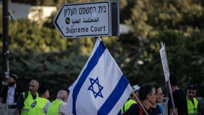people holding large flag of Israel in front of street sign pointing to supreme court