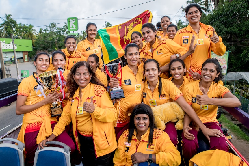 The Sri Lankan netball team pose with a large gold trophy while on an open-top bus.