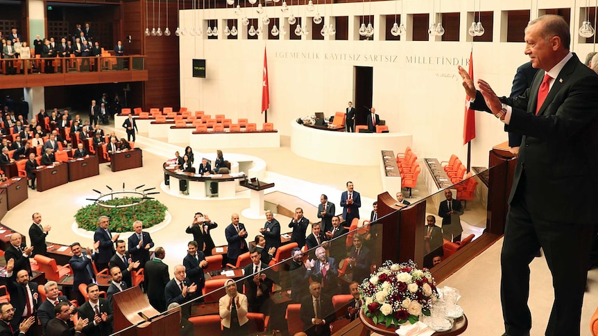 Turkish President Tayyip Erdogan waves to politicians standing below him in parliament