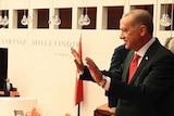 Turkish President Tayyip Erdogan waves to politicians standing below him in parliament