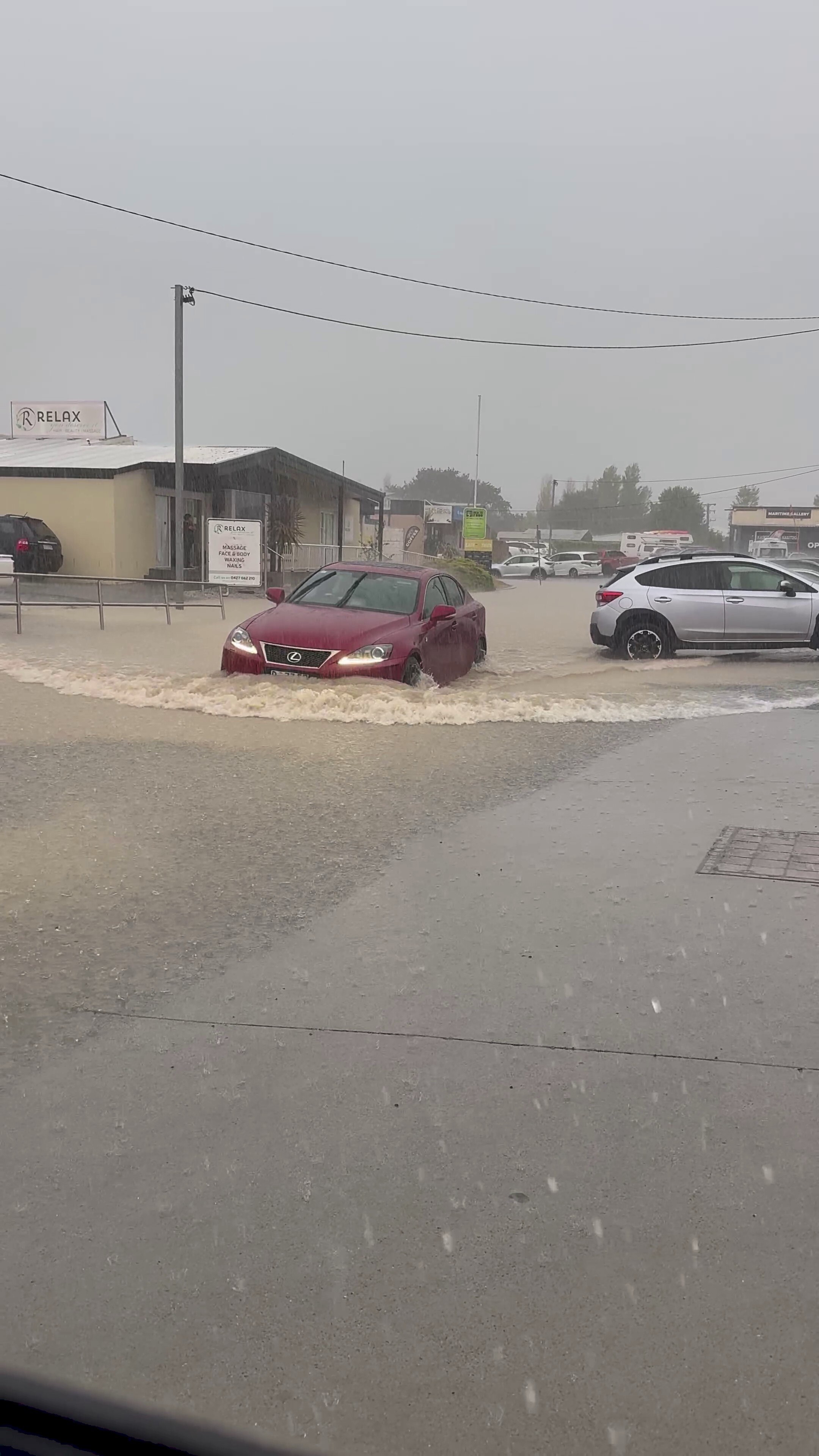 A red sedan drives through floodwaters.