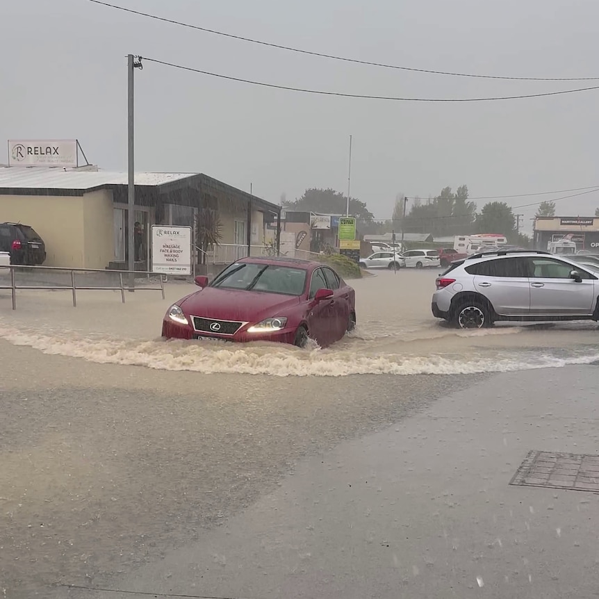 A red sedan drives through floodwaters.