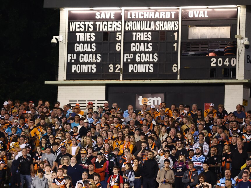 Wests Tigers fans in front of the Leichhardt Oval scoreboard during an NRL game.