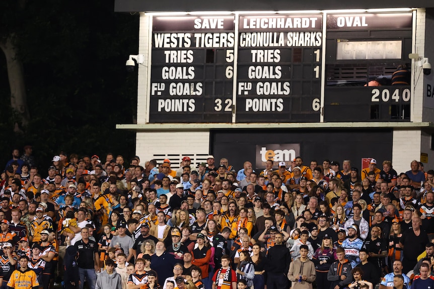 Wests Tigers fans in front of the Leichhardt Oval scoreboard during an NRL game.
