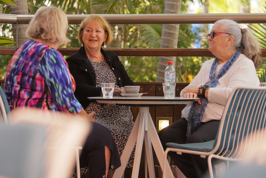 Three older women sit at a table chatting.