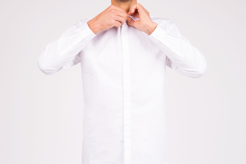 A man does up the top button of a white dress shirt.