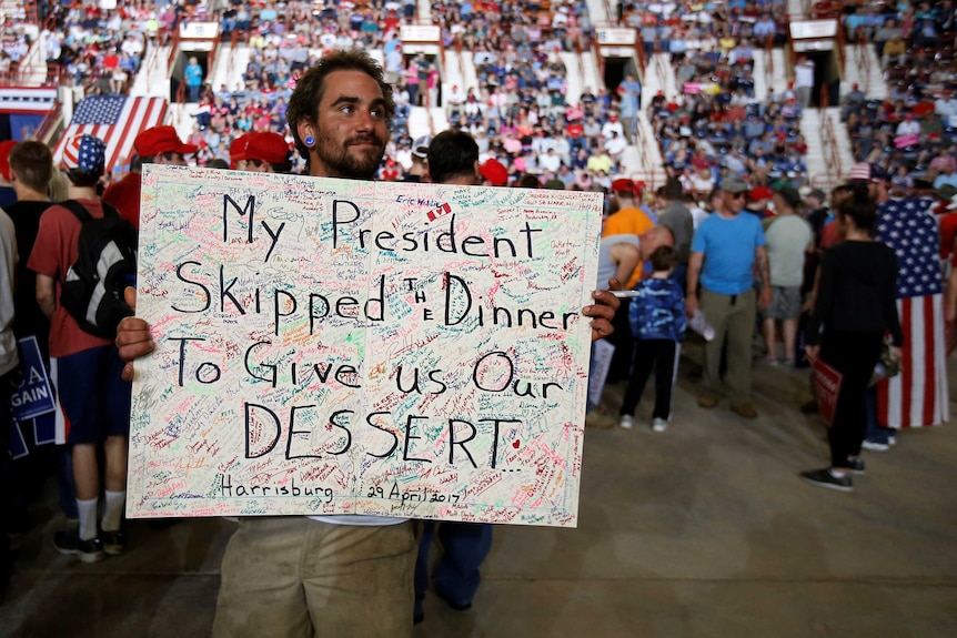 A man holds a sign reading "My President Skipped the dinner to give us our dessert"