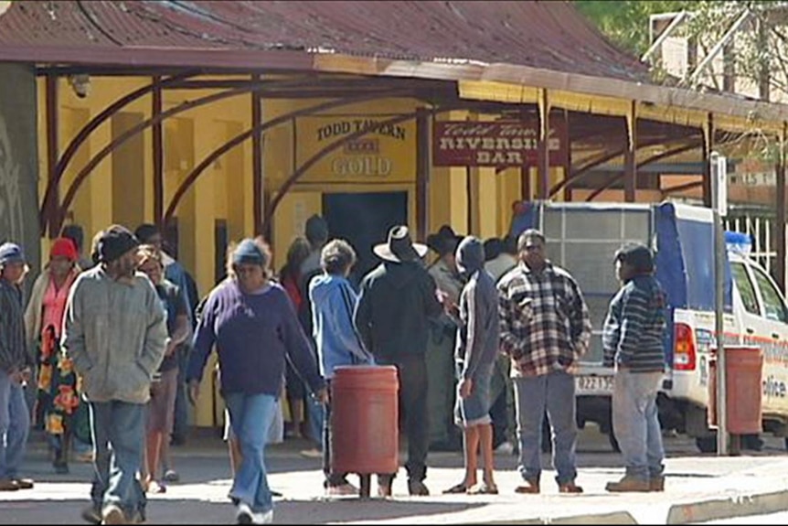 A group of people standing outside a pub on a sunny afternoon.