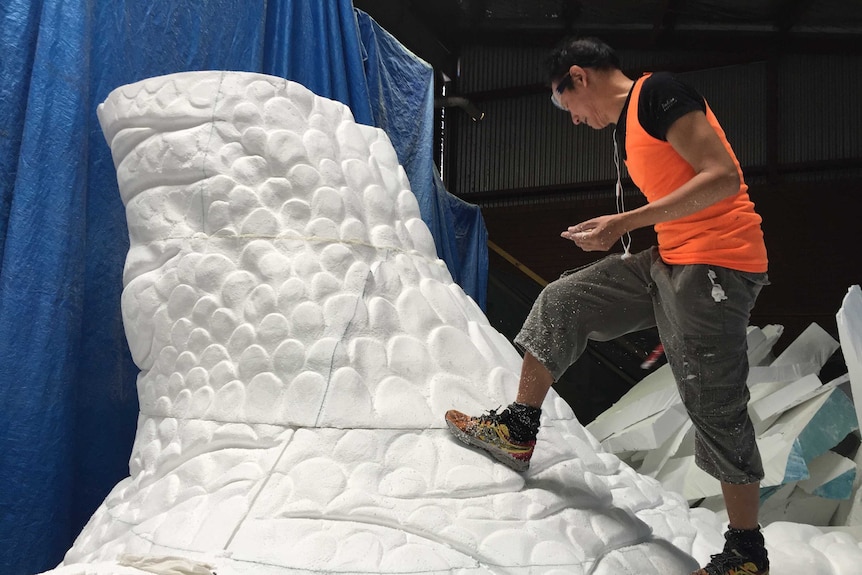 A man climbing on a section of a dragon sculpture.