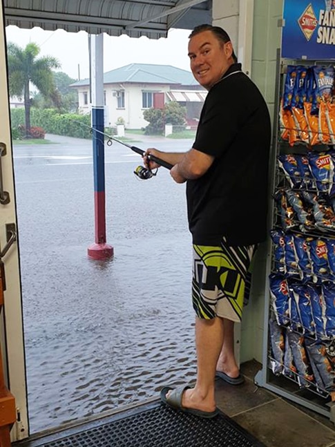 Robert Hutton holds a fishing rod outside flooded entrance to his store the Burdekin Seafood Hut in Ayr.