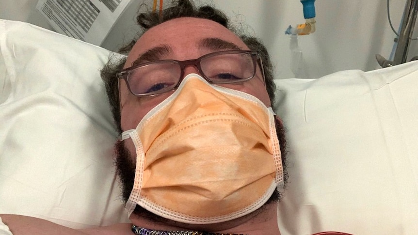 A man lays in hospital with a face mask.