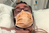 A man lays in hospital with a face mask.