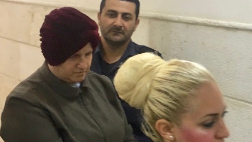 Malka Leifer, bowing her head, is walked into Jerusalem's District Court. Two police officers are also in the photo