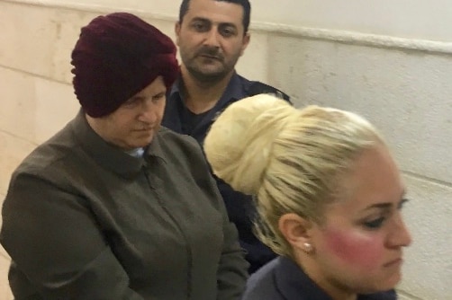 Malka Leifer, bowing her head, is walked into Jerusalem's District Court. Two police officers are also in the photo