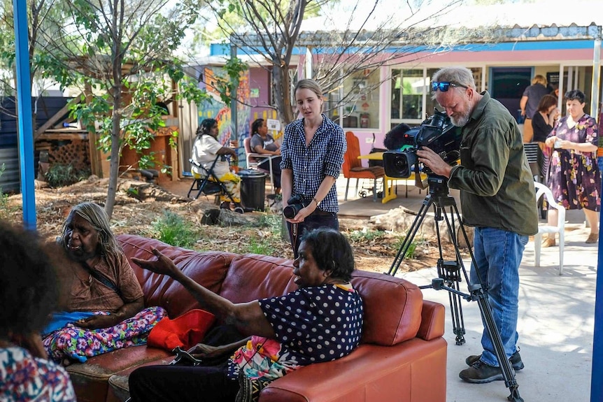 O'Brien holding stills camera watching as Redfearn films women sitting on couches.