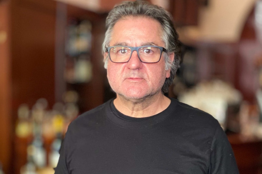 A middle aged man wearing a black t-shirt and square glasses.