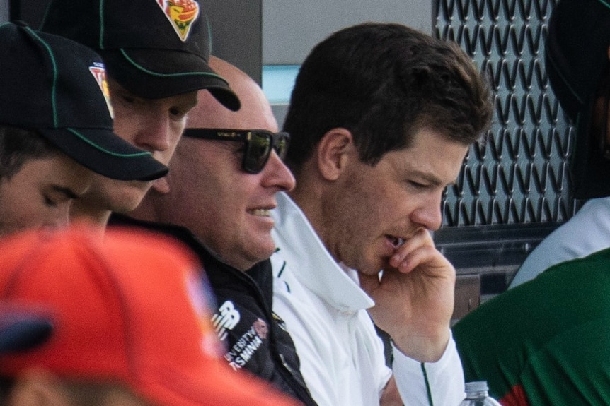 Dominic Baker sits with Tim Paine on the sidelines of a cricket match.