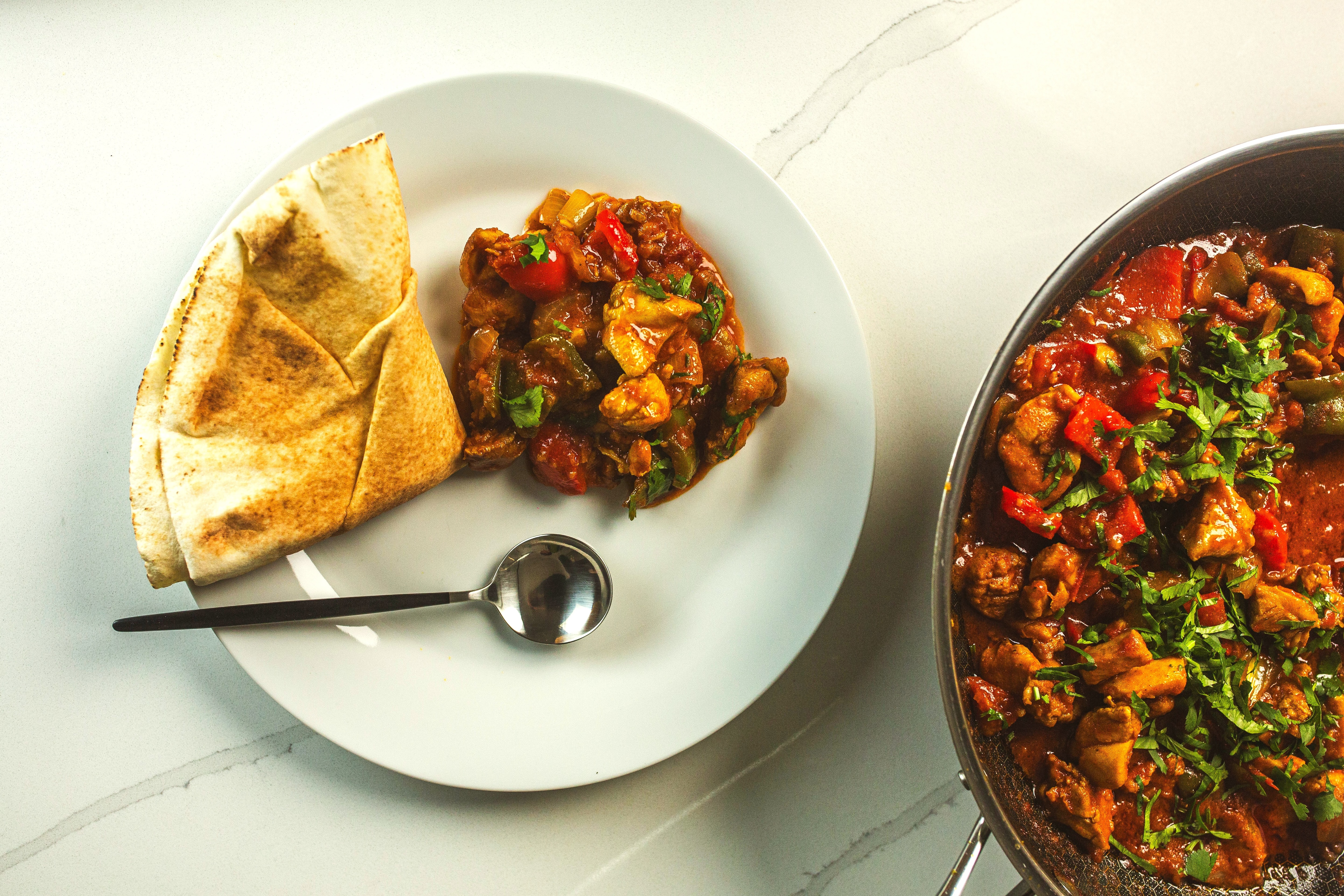 A serving of chicken jalfrezi on a plate with pita bread, the pan of stir fry at the bottom right. A weeknight recipe.