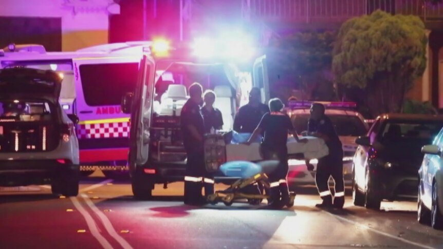 Paramedics load body into ambulance of a man found dead of footpath at Lidcombe in Sydney's west