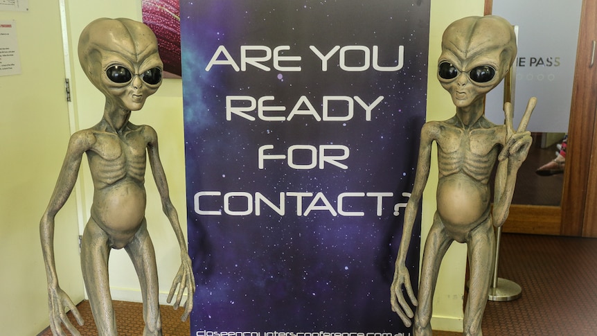 Sign reading 'are you ready for contact' alongside two alien statues