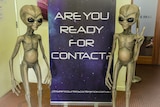 Sign reading 'are you ready for contact' alongside two alien statues