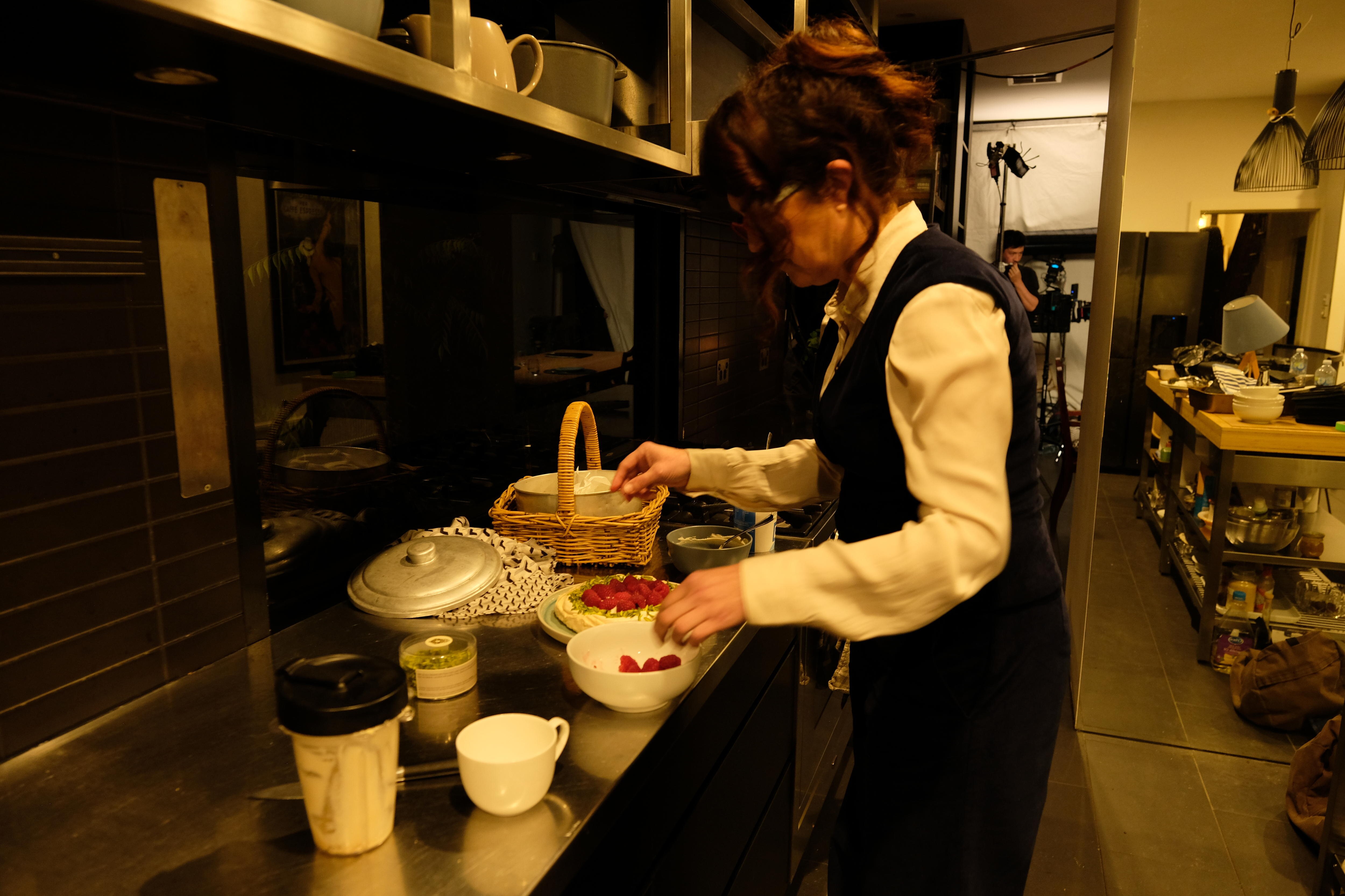 Woman in kitchen putting berries on a dessert with a basket next to her.