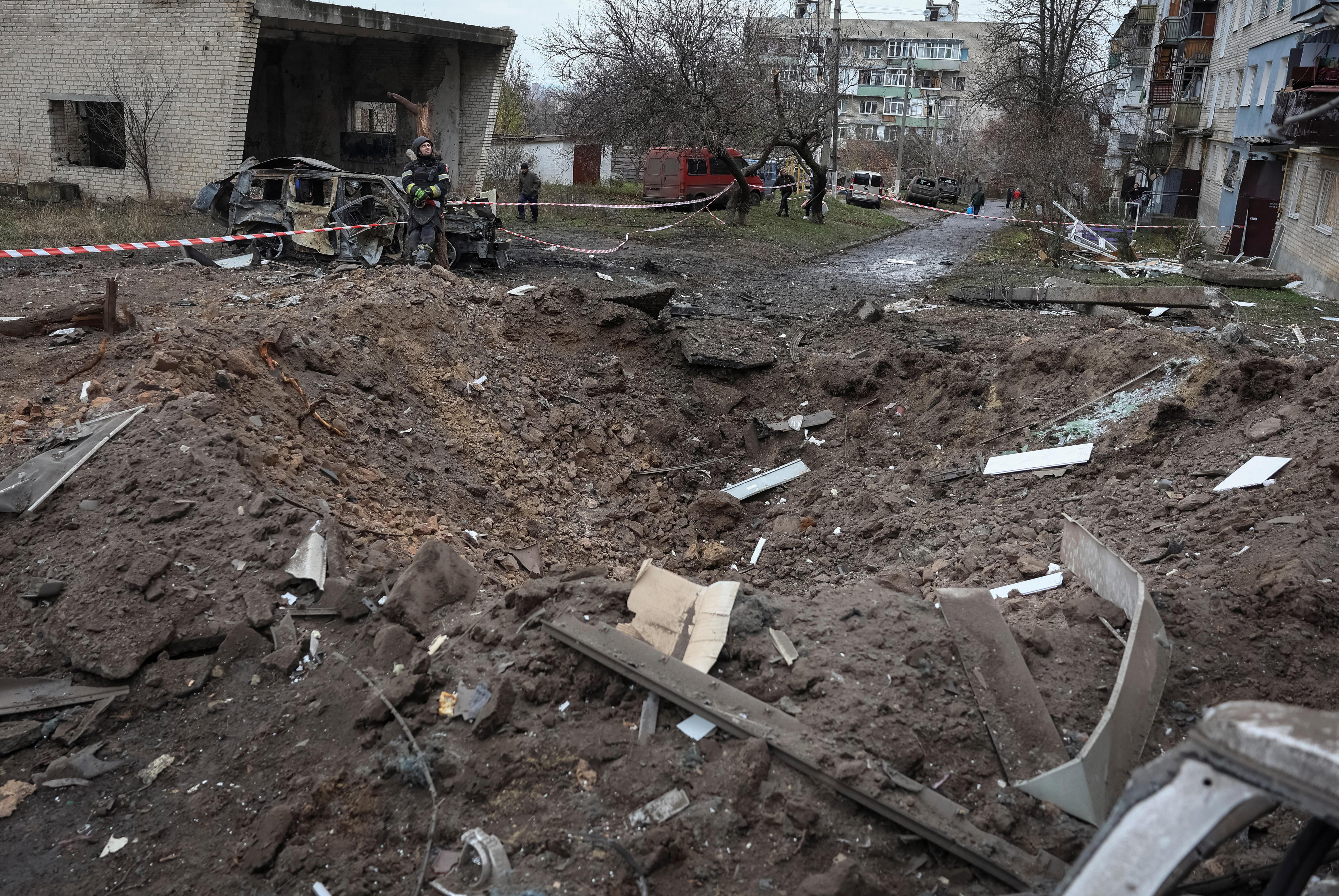 A large blast crater in the ground between two Soviet-era apartment buildings.