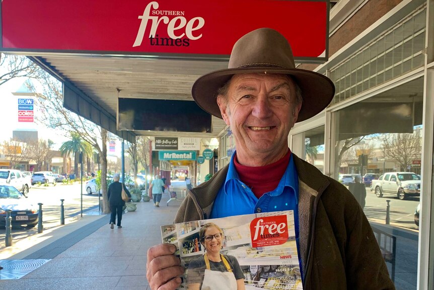 A man wearing an akubra hat holding up a newspaper.