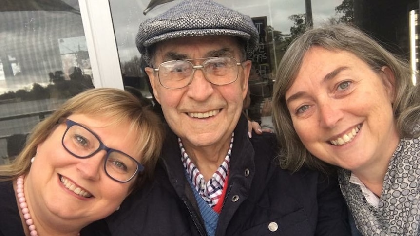 A man with his two adult daughters, all smiling.