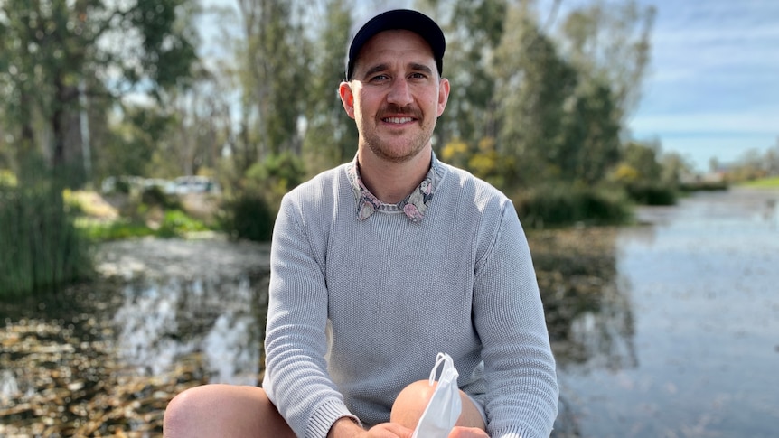 A man in a cap sitting by a creek