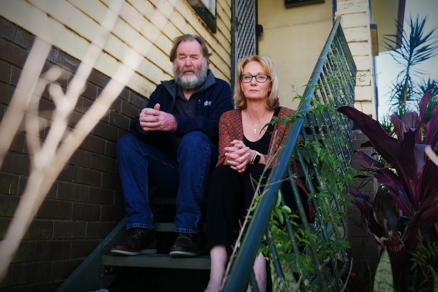 A blonde woman with glasses and a woman with grey hair and beard sitting on steps