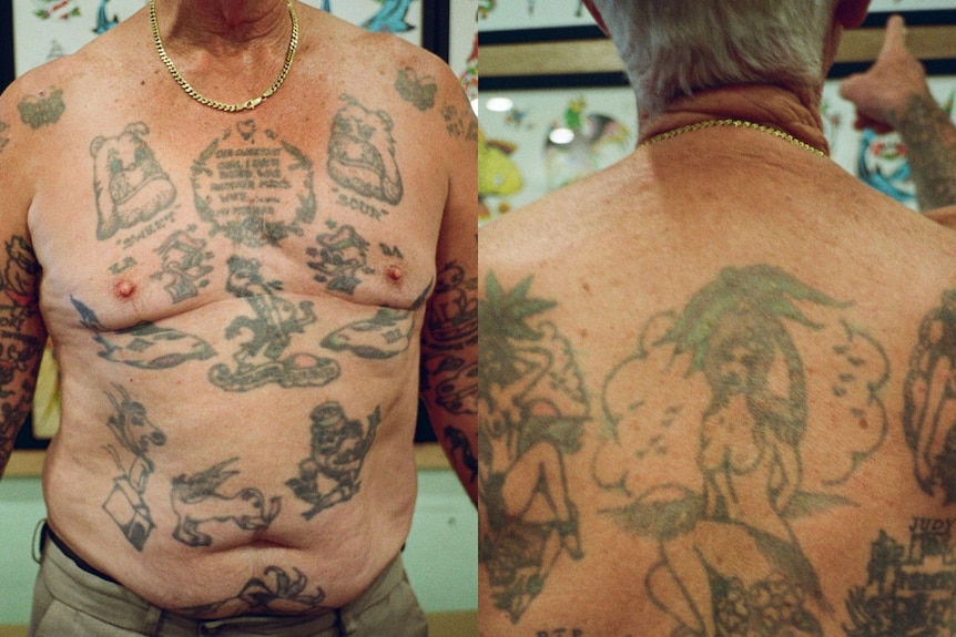 A man shows his bare chest, covered in old tattoos and wears a gold chain. 