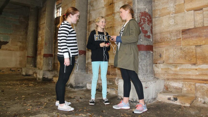 Three girls listening to a historical smart phone app on their phones in a historical building.