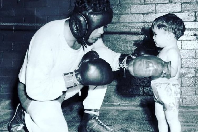 A black and white image of a boxer in gloves playing with a toddler, also in boxing gloves.