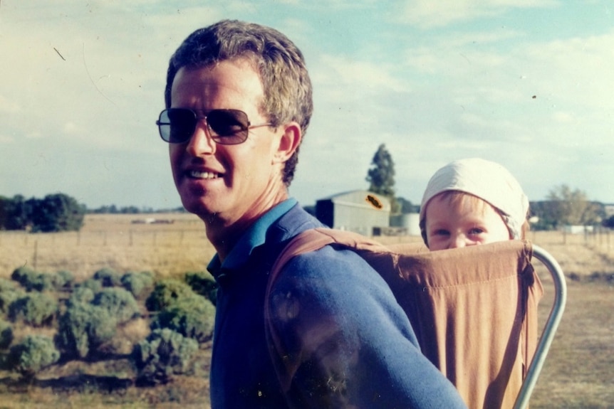 A man wearing sunglasses carrying a baby on his back.